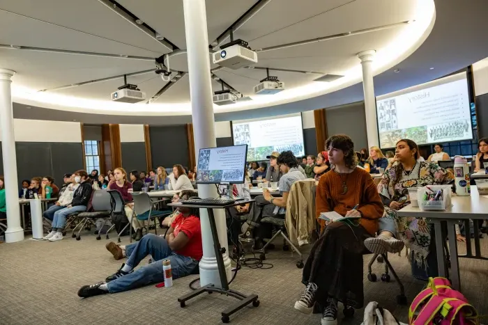 A wide shot of a classroom and many students sitting facing forward.