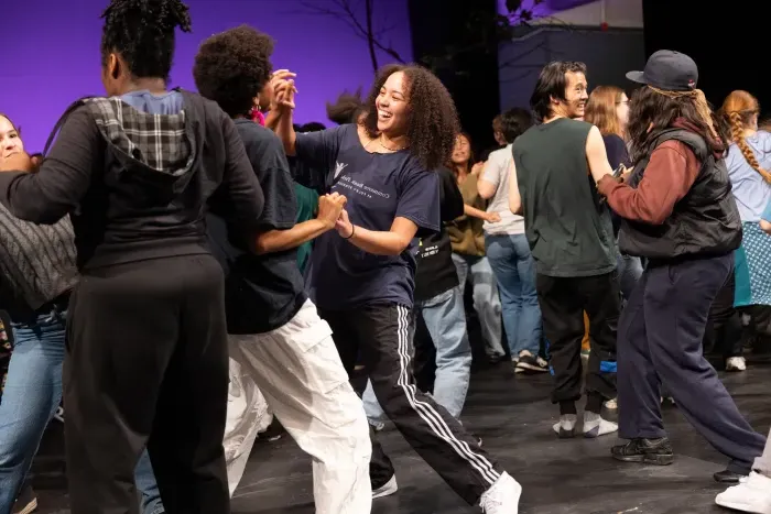 Two students smiling and looking at each other, holding hands as they dance on a stage